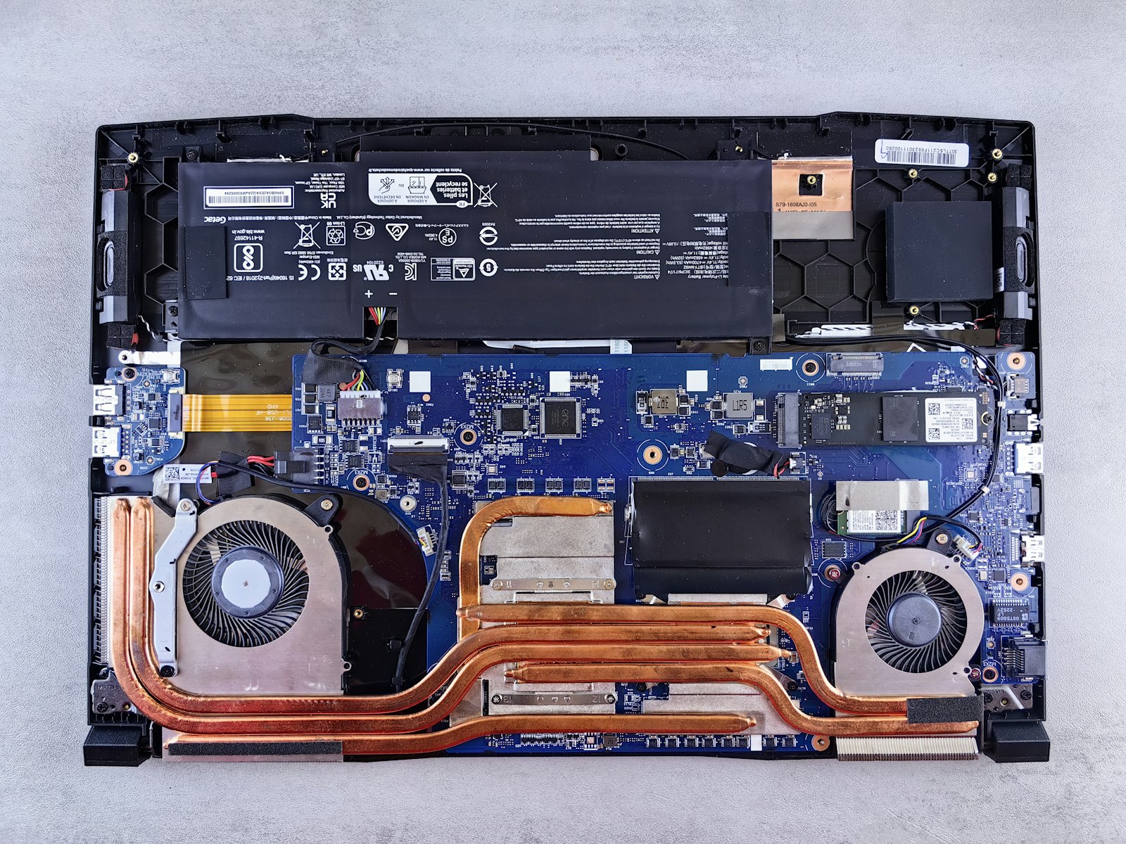 Notebook aberto na bancada mostrando placa, ventoinhas, SSD e bateria